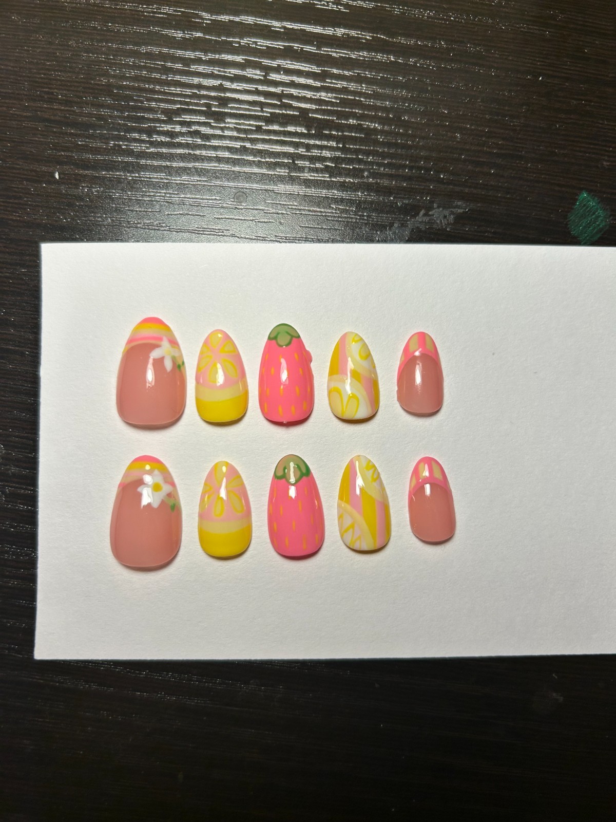Pink and yellow strawberry nail art with pink and yellow swirls and green leaf