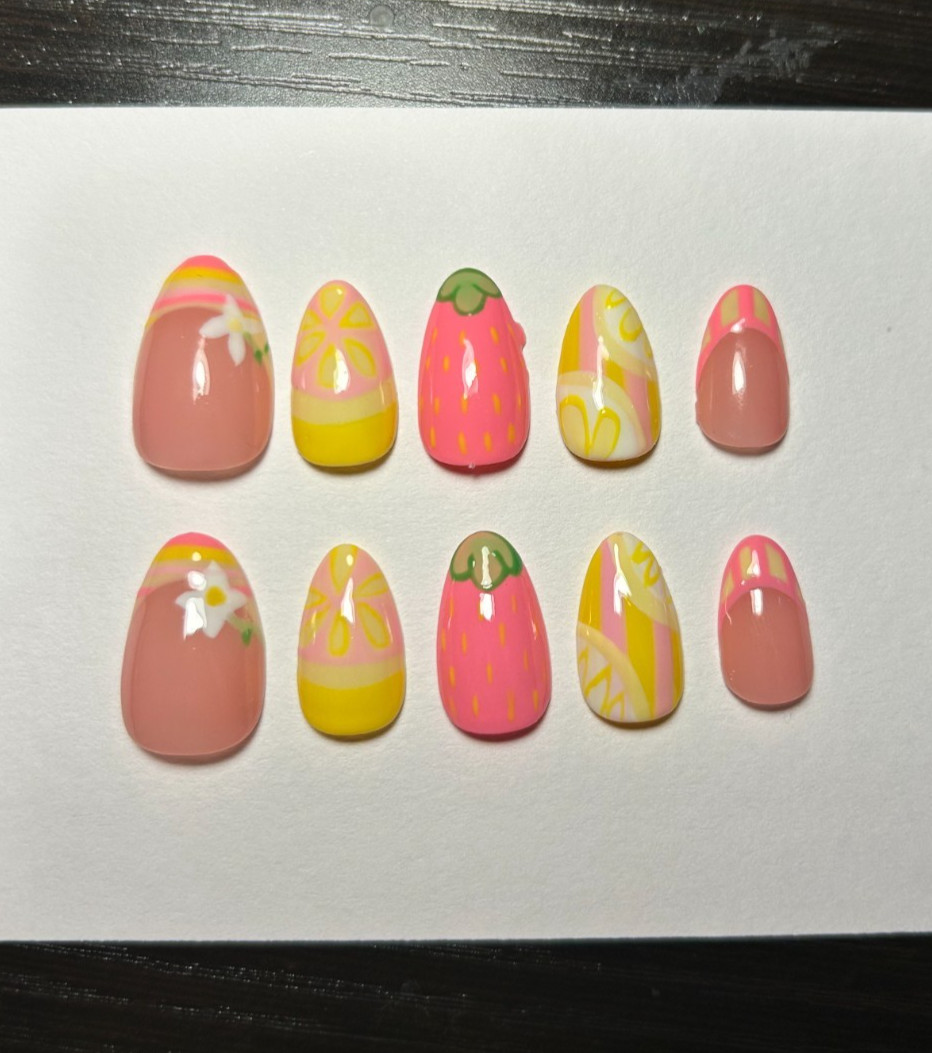 Pink and yellow strawberry nail art with pink and yellow swirls and green leaf